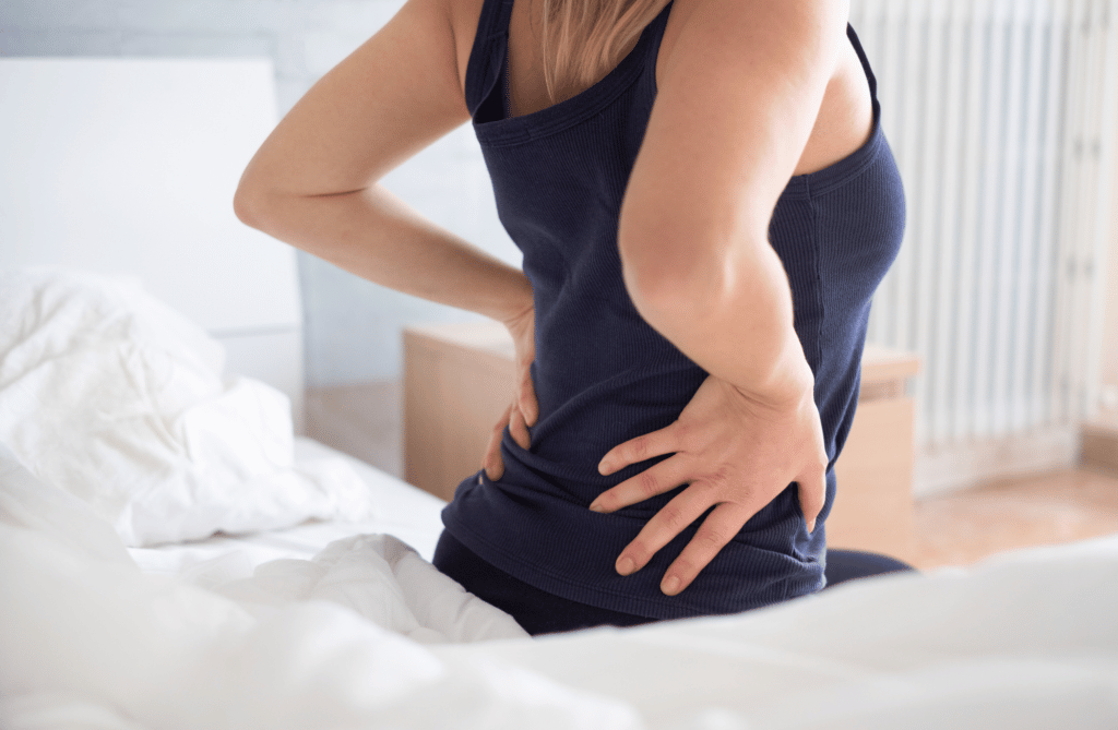 Woman Sitting On Bed With Lower Back Pain